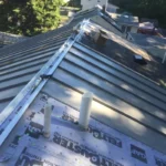 Close-up of metal roof coping installed on a flat roof parapet wall, showing a sleek, protective cap directing water away from the structure.